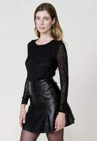 Top nero a maniche lunghe con ricamo floreale, abbinato a una mini gonna in pelle nera, caratterizzata da una forma svasata e una fessura frontale.