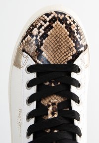 Sneaker in pelle bianca con lacci neri, dotata di una punta in vernice di serpente lucido con motivo in marrone e nero, e un accento dorato sul tallone.