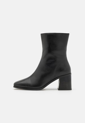 Bottines en cuir noir, bout pointu, texture lisse, talon bloc de hauteur intermédiaire, design minimaliste et finitions cousues le long du col.