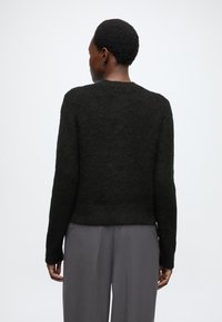 Czarny, teksturowany sweter z długimi rękawami i okrągłym dekoltem, zestawiony z szarymi, szerokimi spodniami. Minimalistyczny design o czystych liniach.