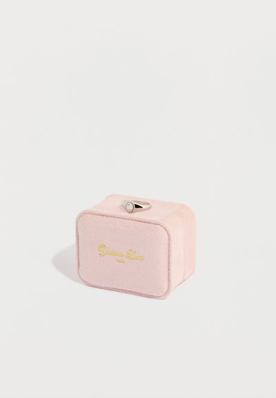 Ροζ βελούδινο κουτί κοσμημάτων με απαλή υφή, ορθογώνιο σχήμα και ανάγλυφο χρυσό λογότυπο. Περιέχει ασημένιο δαχτυλίδι στην κορυφή με διακοσμητική πέτρα.