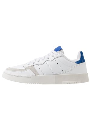 Hvid lav sneakers med blå hælkappe, perforerede detaljer på siden, hvide snørebånd og en tyk tekstureret sål.