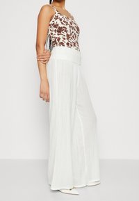 Bílé široké kalhoty vyrobené z texturované, splývavé látky. V kombinaci s pěkně padnoucím topem s hnědým a bílým květinovým vzorem, který má tenké ramínka.