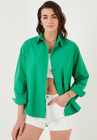 Green button-up shirt in lightweight fabric with long sleeves, relaxed fit, and white shorts. Features a classic collar and rolled cuffs.