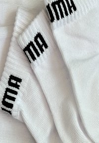 White cotton socks featuring a ribbed texture and black embroidered logo on the cuff. Three socks are stacked overlapping slightly.