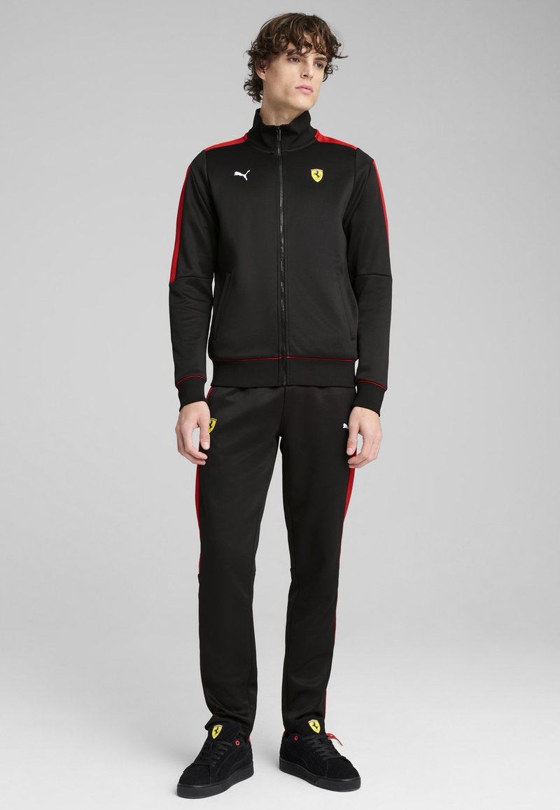 Zwarte trainingspak met rode zijstrepen, met een ritssluiting jas en ribgebreide manchetten. Bevat Puma- en Ferrari-logo's. Zacht, lichtgewicht materiaal.