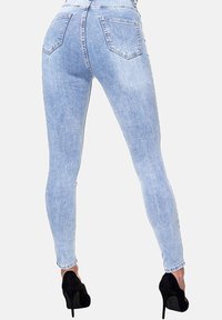 Jeans ajustados azul claro con un acabado desgastado, que cuentan con dos bolsillos traseros y una cintura alta. Combinados con zapatos de tacón negro.