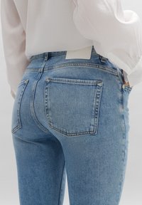 Jean en denim bleu clair au design ajusté. Dispose de deux poches arrière, de coutures discrètes et d'une étiquette blanche au niveau de la taille.