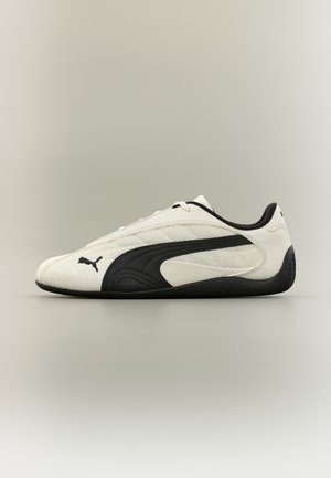 Fehér és fekete Puma alacsony szárú sportcipő texturált talppal és Puma logóval az oldalon, semleges, egyszínű háttér előtt.