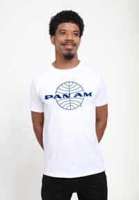 Bílý bavlněný tričko s modrým logem "PAN AM" a designem globu na přední straně. Krátké rukávy a kulatý výstřih. Jednoduchý, čistý design.