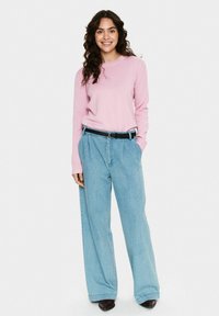 Pull en maille rose clair à manches longues, coupe décontractée, associé à un pantalon en denim bleu clair à jambe large et une ceinture noire. Texture lisse, design décontracté.