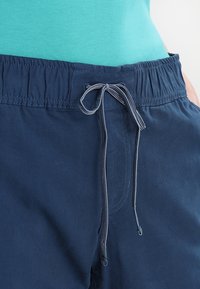 Pantaloni corti blu navy con vita elastica, dotati di cordoncino e superficie liscia. Abbinati a una maglietta turchese chiaro.