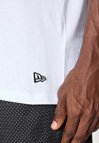 T-shirt en coton blanc avec un petit logo noir brodé au bas ; associé à un short en mesh noir texturé présentant un motif à pois.