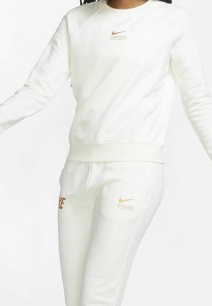 Persona con sudadera y pantalones deportivos blancos de Nike, ambos con pequeños logotipos de Nike de color naranja claro y elementos gráficos.