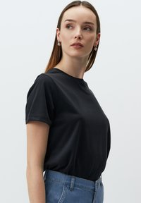 Czarny krótki rękaw t-shirt z gładkiego materiału. Okrągły dekolt i luźny krój, zestawiony z niebieskimi jeansami o wysokim stanie.