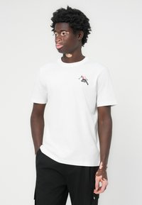 Weißes Baumwoll-T-Shirt mit Rundhalsausschnitt und kurzen Ärmeln. Auf der Brust befindet sich ein farbenfrohes Motiv einer sich bewegenden Figur.