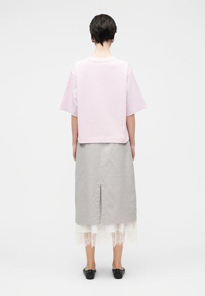 Κοντομάνικο, ανοιχτό ροζ τοπ με κουτί σχεδίασης, συνδυασμένο με γκρι φούστα που διαθέτει ανοίγμα στο πίσω μέρος και στρώσεις λευκής δαντέλας στο τελείωμα.