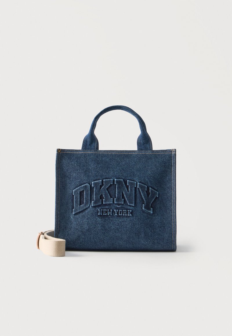 Sac cabas en denim avec des anses courtes, brodé de "DKNY New York" sur le devant, et une bandoulière beige amovible à côté.