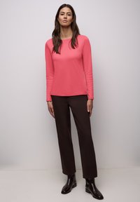 Camisa de manga larga en coral brillante, confeccionada en tela suave, combinada con pantalones marrones y botines negros brillantes. Diseño sencillo y ajustado.