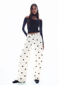 Fekete hosszú ujjú felső, fehér, széles szárú nadrággal, nagy fekete pöttyökkel díszítve. Az öltözék testhez simuló szabású és sima textúrájú.