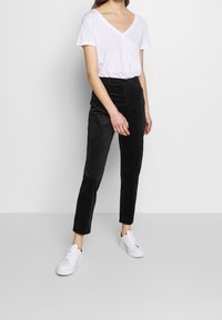 Svarta sammetbyxor med slim fit, hög midja och avsmalnande ben, i kombination med en vit t-shirt med v-ringning och vita sneakers.