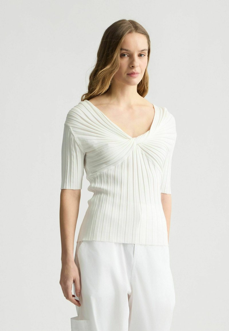 Top bianco a coste con maniche corte, caratterizzato da scollatura a V e texture drappeggiata sulla zona del busto, finitura liscia e vestibilità comoda.