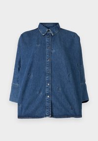 Denim krekls ar klasisku apkakli, zilā krāsā, pārmērīgā izmērā un dekoratīvām sirds formas izgriezumiem. Aprīkots ar snap pogām un garām piedurknēm.