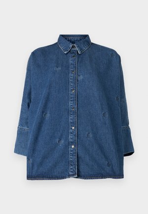 Denim särg klassikalise kaelusega, sinine värv, oversized lõige ja dekoratiivsete südamekujude lõigetega. Omab nupuleheket ja pika varrukaga disaini.