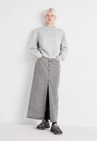Sivá mikina a dlhá sivá džínová sukňa s predným rozparením. Skombinované s čiernymi a sivými teniskami. Jednoduchý, ležérny outfit na bielom pozadí.