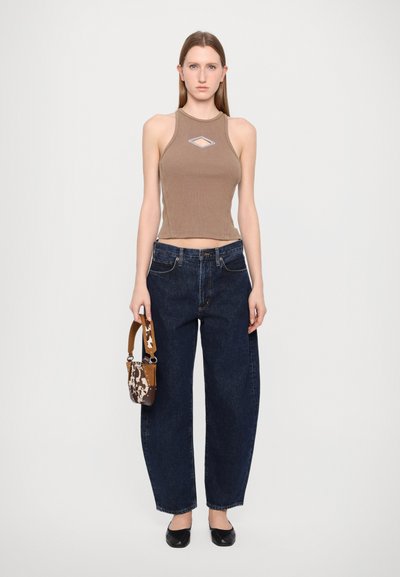 Braun gerippter Crop-Top mit einem diamantförmigen Ausschnitt, blaue hochtaillierte, weite Jeans, schwarze Ballerinas und eine kleine gemusterte Handtasche.