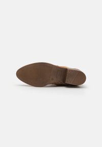 Suela de zapato de cuero marrón con una superficie texturizada y surcos para tracción. Presenta un pequeño detalle rectangular y una puntera redondeada.