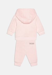 Survêtements en velours rose avec un hoodie et des poignets élastiques. Présente le logo "BOSS" sur le pantalon, une texture douce et une coupe décontractée.