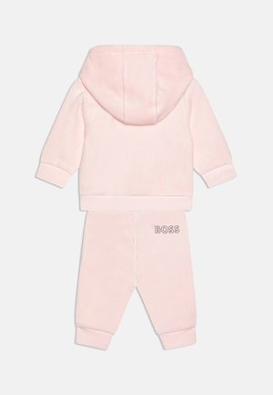 Survêtements en velours rose avec un hoodie et des poignets élastiques. Présente le logo "BOSS" sur le pantalon, une texture douce et une coupe décontractée.
