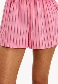 Shorts rayés roses avec des lignes verticales dans des nuances de rose, jaune et marron. Caractéristiques d'une coupe décontractée et d'une texture douce près de l'ourlet.