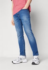 Tajta blå denimjeans med en lätt sliten yta, försedd med fem fickor och subtila sömdetaljer. Matchade med vita sneakers.