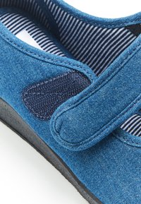 Zapato de tela azul con cierre de velcro, que presenta un parche textil marino, forro interior a rayas y suela de goma negra sólida.