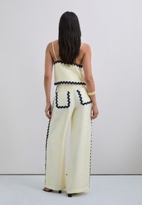 Yellow two-piece outfit featuring a cropped top with ruffled navy trim and wide-leg pants with pocket details and side accents.
