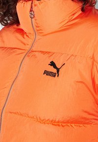 Giacca piumino Puma di un vivace arancione con una texture lucida, con zip completa e logo nero sul petto; presenta un colletto arricciato.