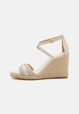 Sandale compensée avec une tige en cuir crème, une sangle en tissu à motifs et une semelle en jute tissée. Sangle cheville réglable avec détail de boucle en or.