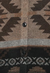 Cardigan marrón con estampado de diseños geométricos, dos botones negros en el centro y una textura suave similar a la lana.