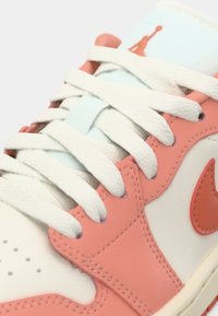 Baskets blanches avec des accents corail, en cuir texturé, avec des lacets plats et une languette bleu clair ornée d'un logo Jumpman.