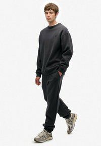 Mørkegrå sweatshirt med rund hals og løs pasform, parret med matchende sweatpants. Materialet ser blødt ud med en tekstureret overflade.