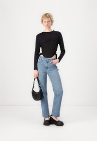 Zwarte lange mouw top met een getailleerd ontwerp, hoge taille blauwe jeans, zwarte chunky platform schoenen en een kleine zwarte handtas met studs.