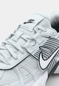 Valged Nike tossud, millel on tekstuuriga ülemine osa, mustad aktsendid, eristuvad külgpaneelid ja silmatorkav logo keele peal.