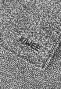 Grey textured fabric with a woven pattern, featuring the embroidered word "KIWEE" in black. The corner is folded, revealing seam details.