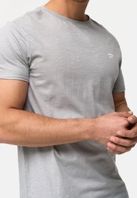 T-shirt court à manches courtes de couleur gris clair, fabriqué en tissu doux, avec un petit logo blanc sur la poitrine et un col rond classique.