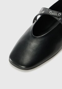 Zwarte leren schoen met een vierkante neus en uitsnijdingen; heeft een kruisbandontwerp met metalen oogjes. Glad oppervlak.