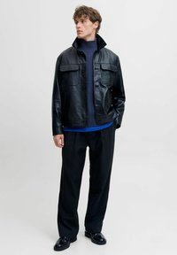 Chaqueta de cuero negra con dos bolsillos en el pecho, combinada con un suéter de punto azul marino, pantalones negros a rayas y mocasines negros.