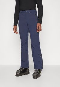 Μπλε σκούρα σαλοπέτα σκι κατασκευασμένη από υλικό αδιάβροχο. Χαρακτηριστικά περιλαμβάνουν τσέπες με φερμουάρ, ενισχυμένες ραφές και ευθεία γραμμή.