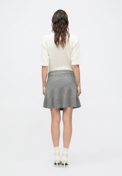 Krótki kremowy sweter z krótkim rękawem w połączeniu z szarą rozkloszowaną spódnicą. Modelka nosi białe skarpetki do kostek i szpilki, prezentując prosty, codzienny zestaw.